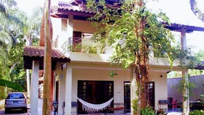 A two-story house with a balcony, a hammock, and a car parked in front. - Nice house just 330 feet away from the beach (São Sebastião)