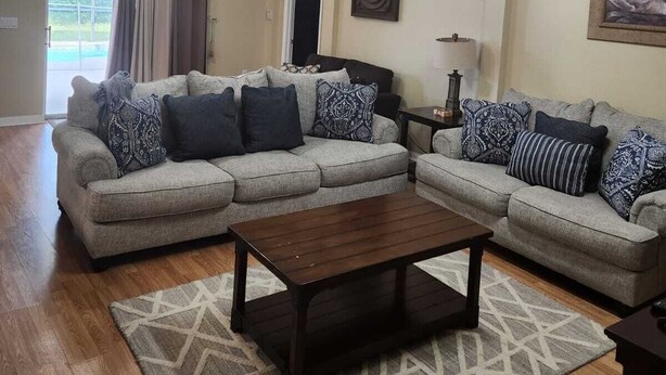 A living room with a sectional sofa, a coffee table, a ceiling fan, and a chandelier.
