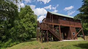 A wooden treehouse with a balcony and stairs, surrounded by lush greenery. - Beautiful Romantic River front cabin with mountain views,fantastic location! (Luray)