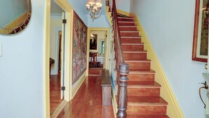 A staircase with wooden steps and a red handrail, leading to a room with a chandelier and a large mirror on the wall.