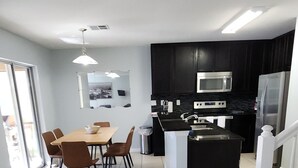 A modern kitchen with dark cabinets, a central island, and a dining area with a table and chairs.