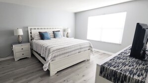 A bedroom with a bed, nightstands, a lamp, a TV, and a window.