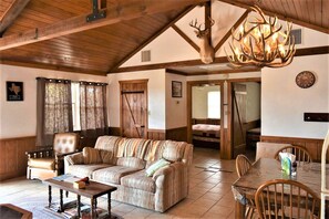 A rustic interior with a wooden ceiling, a sofa, a dining table, and a chandelier.