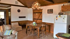 A cozy living room with a wooden dining table, chairs, a sofa, and a kitchen area with a refrigerator and wooden cabinets. - Maner Lodge getaway, views from 1 of highest elevation pts, BBQ, 30min FBG (Doss)