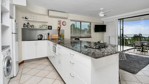 A modern kitchen with white cabinetry, a granite countertop, and a built-in washing machine. - Best Location in Cairns - Ocean Views (Cairns)