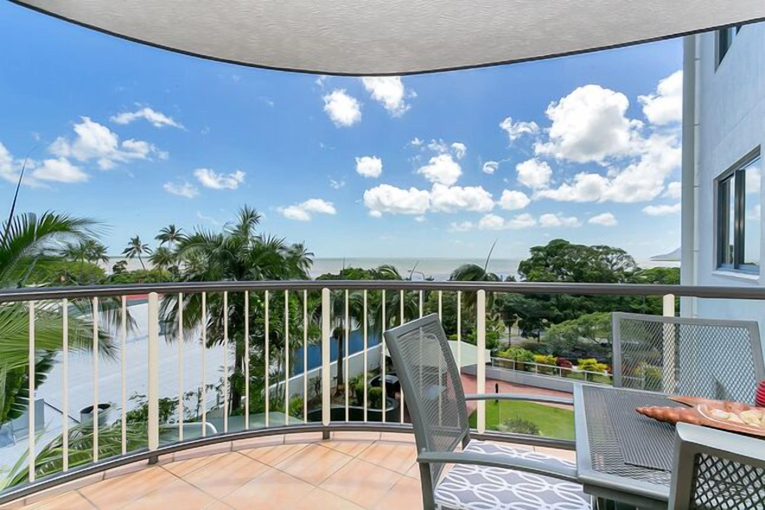 Een balkon met een gebogen reling, een tafel met stoelen en uitzicht op een zwembad en groen.
