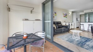 A modern living room with a black leather sofa, a dining table with metal chairs, and a kitchen area visible through an open door. - Best Location in Cairns - Ocean Views (Cairns)