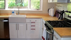 A kitchen with white cabinets, a stainless steel dishwasher, a gas stove, and a window with a view of greenery.