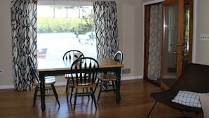 A dining area with a table and chairs, a view of a body of water, and a door leading outside.