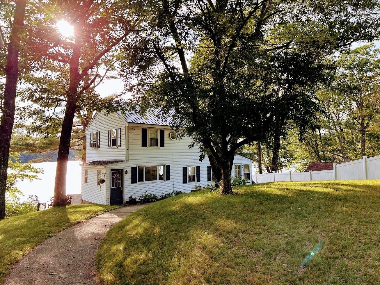 A two-story white house with a front porch, a pathway leading to the entrance, and a white fence surrounding the property.