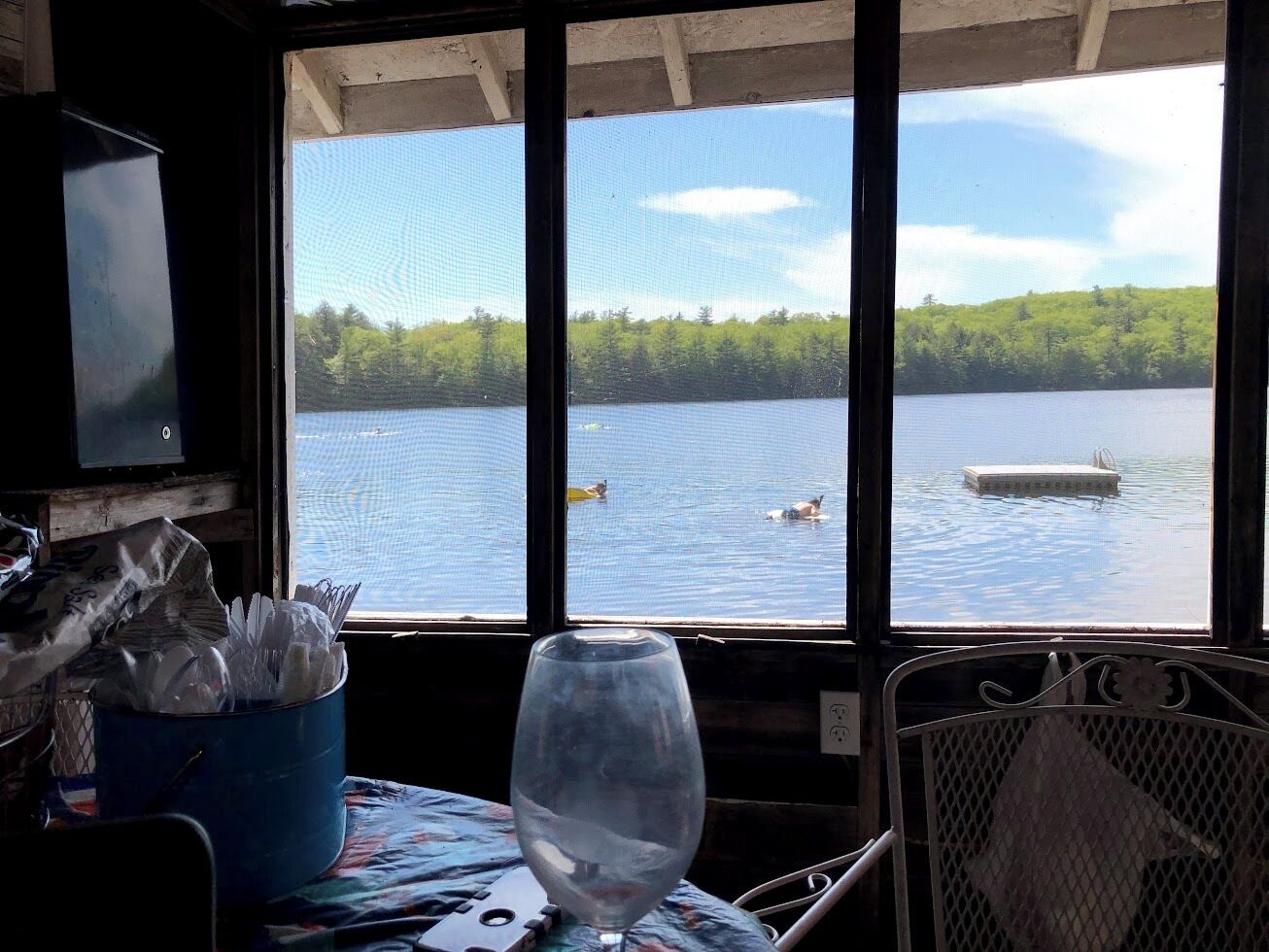 A room with a large window overlooking a lake, a table with a glass, and a chair.