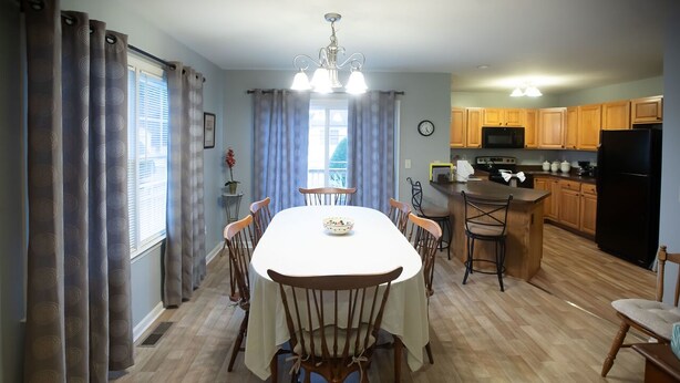 A dining area with a table and chairs, a kitchen with wooden cabinets, a microwave, and a refrigerator.