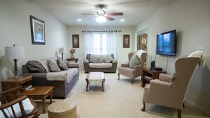 A living room with a ceiling fan, two couches, a coffee table, a TV, and a bookshelf.