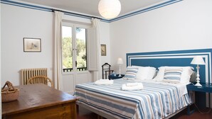 Un dormitorio con cama, mesita de noche, lámpara y vistas al exterior por una ventana.