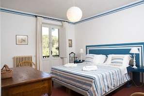 Een slaapkamer met een bed, nachtkastje, lamp en uitzicht op het groen buiten.