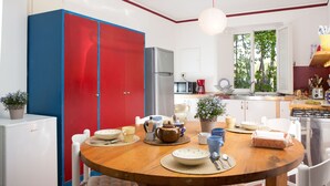 Una cocina compacta con comedor, con una mesa de madera dispuesta para una comida, un refrigerador y un ventanal con vista a árboles.
