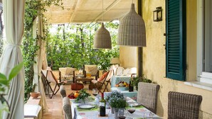 Un área de comedor al aire libre con una mesa preparada para cuatro personas, rodeada de sillas de mimbre y un porche cubierto.
