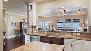 A spacious kitchen with granite countertops, white cabinetry, and a large island. There are pendant lights, a ceiling fan, and large windows providing natural light. - Stunning Waterfront Villa w Incredible Views - Htd Pool, Spa, Dock, Beach, Gm Rm (Mary Esther)