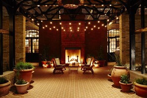 A cozy outdoor seating area with a brick fireplace, potted plants, and string lights. - Walk to Riverwalk & Alamo • Luxury Southtown 3BR • Stylish Home Near Alamodome (San Antonio)