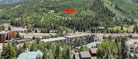 A residential area with a mix of modern and traditional buildings, surrounded by dense forest and mountains.