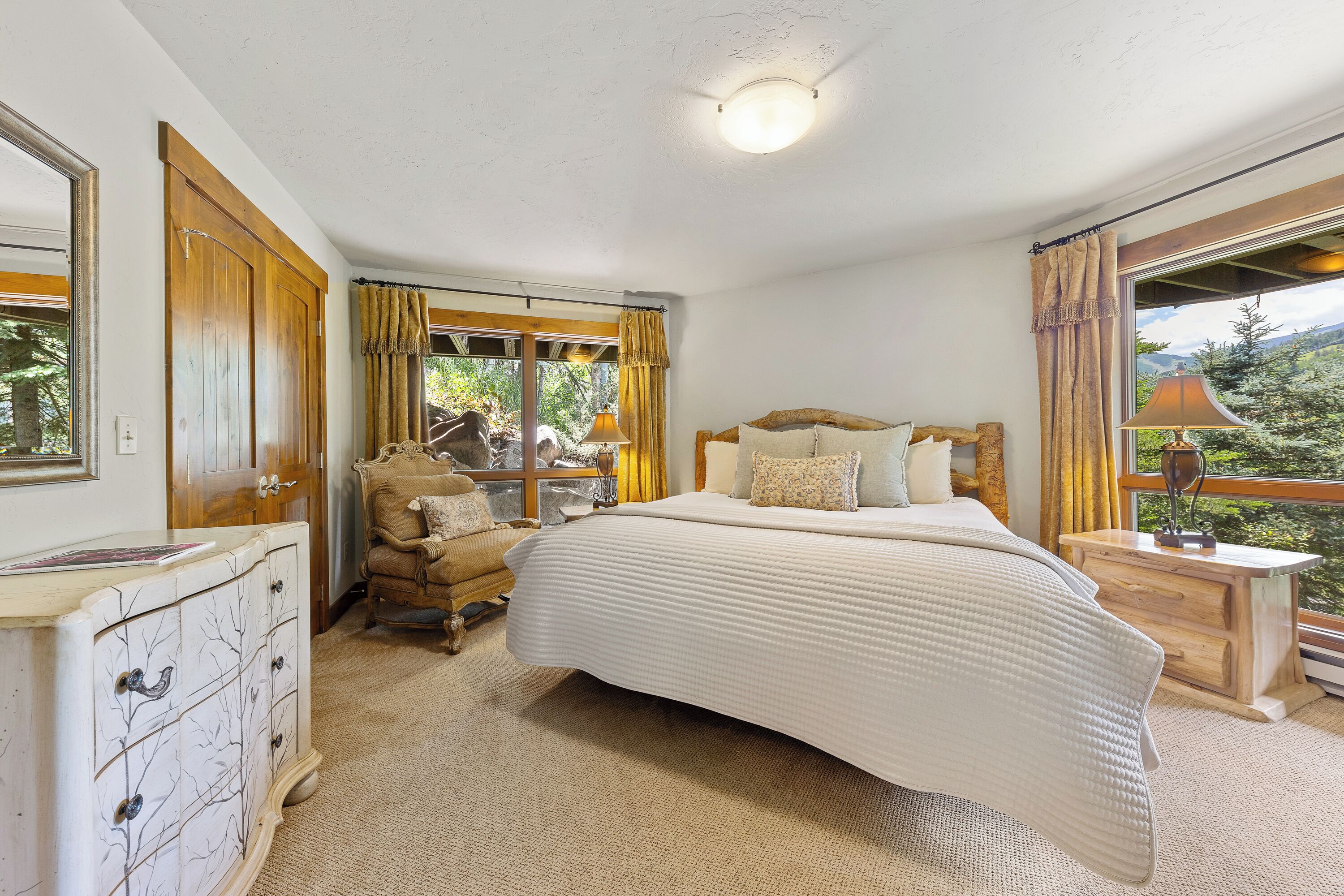 A bedroom with a large bed, a wooden dresser, a chair, and a nightstand with a lamp.