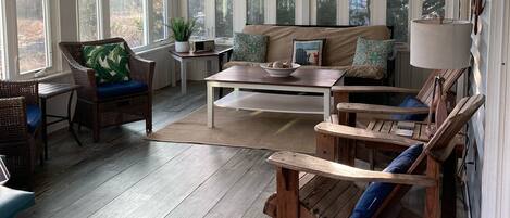 A sunroom with large windows, a ceiling fan, and wooden furniture.