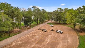 Un’area di parcheggio con una strada sterrata che conduce a un edificio, circondata da alberi.