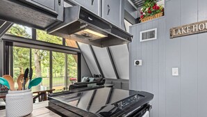 Een moderne keuken met een ruime inductiekookplaat, een inbouwoven en een roestvrijstalen afzuigkap. Er is een raam met uitzicht op groen, en een bord op de muur met de tekst 'LAKE HOUSE'.