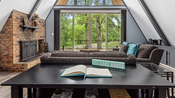 Een gezellige woonkamer met een open haard, een groot raam en een bord met de tekst 'Welcome to our Lake House'.