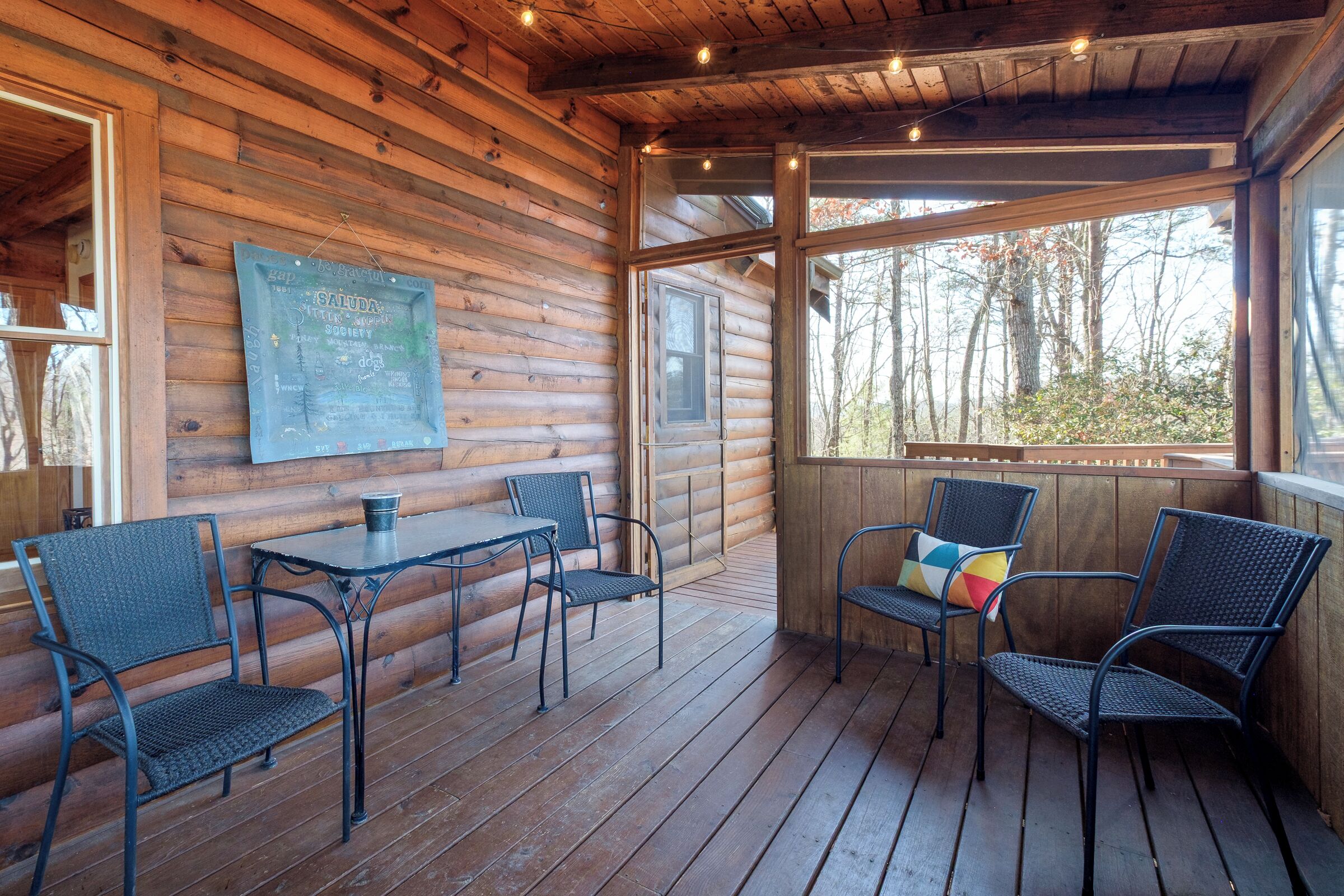 Une cabane en bois dotée d’une terrasse en bois, d’une table avec des chaises et d’un tableau noir sur lequel on a écrit.