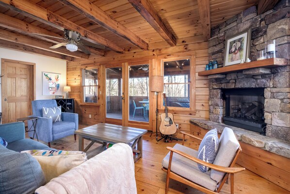 Ein gemütliches Blockhaus-Interieur mit Holzwänden, einem Kamin aus Stein, einer Gitarre und einem Essbereich.