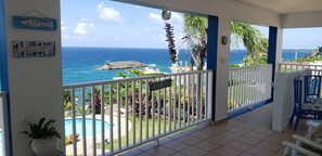 Ein Balkon mit Blick auf den Ozean, ein Pool und tropische Pflanzen.