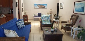 Ein Wohnzimmer mit einem blauen Sofa, einem Korbsessel, einem Couchtisch und einem weißen Tisch mit einer Lampe.