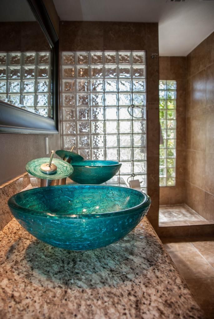 A bathroom with a granite countertop, a glass shower enclosure, and a window with a view of greenery.