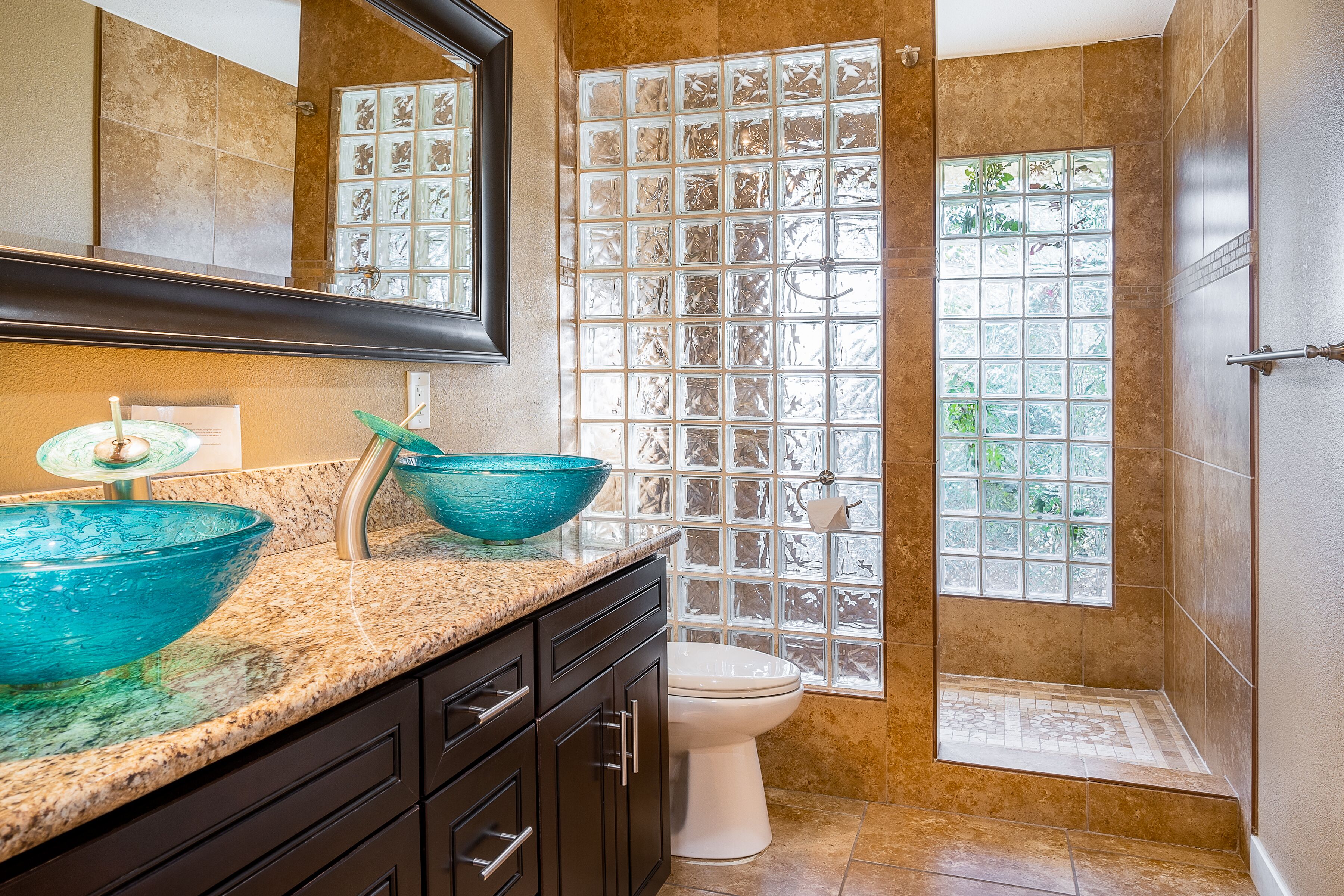 A bathroom with a glass shower enclosure, a sink with a blue glass bowl, and a toilet.