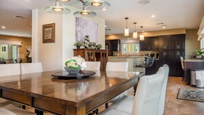 Un comedor amplio con una larga mesa de madera, sillas blancas y una lámpara moderna.
