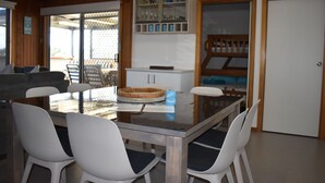 Un coin repas comprenant une table à plateau en verre, des chaises blanches et un buffet en bois contenant de la verrerie.
