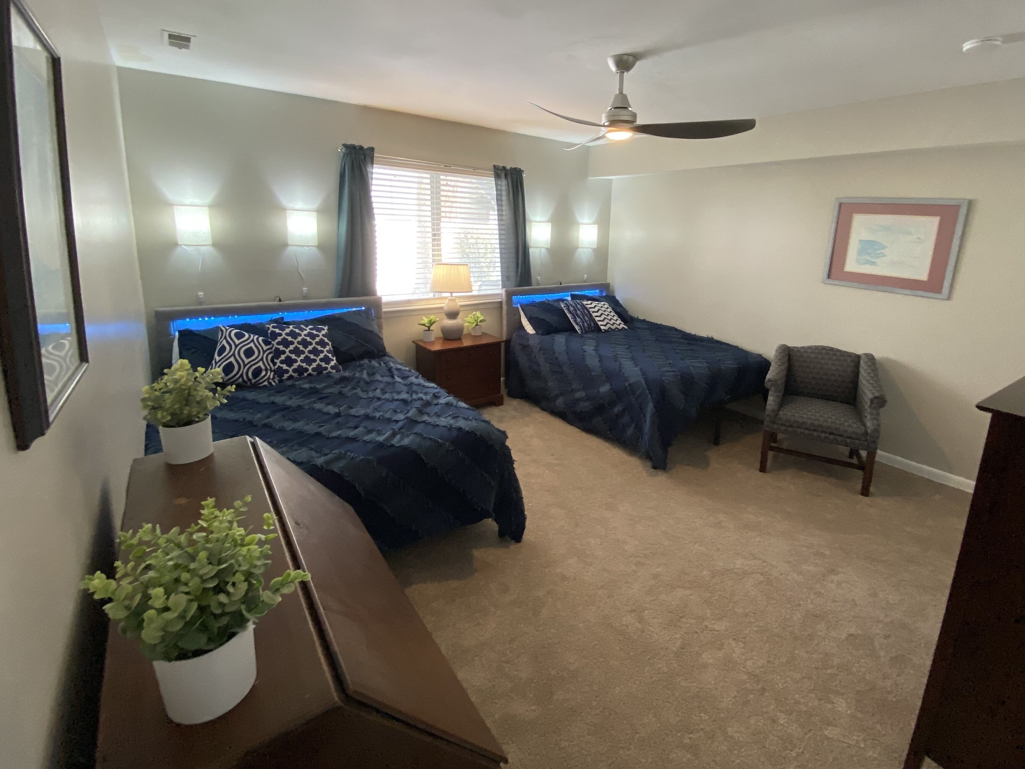 A bedroom with two beds, a ceiling fan, a nightstand with a lamp, and a chair.