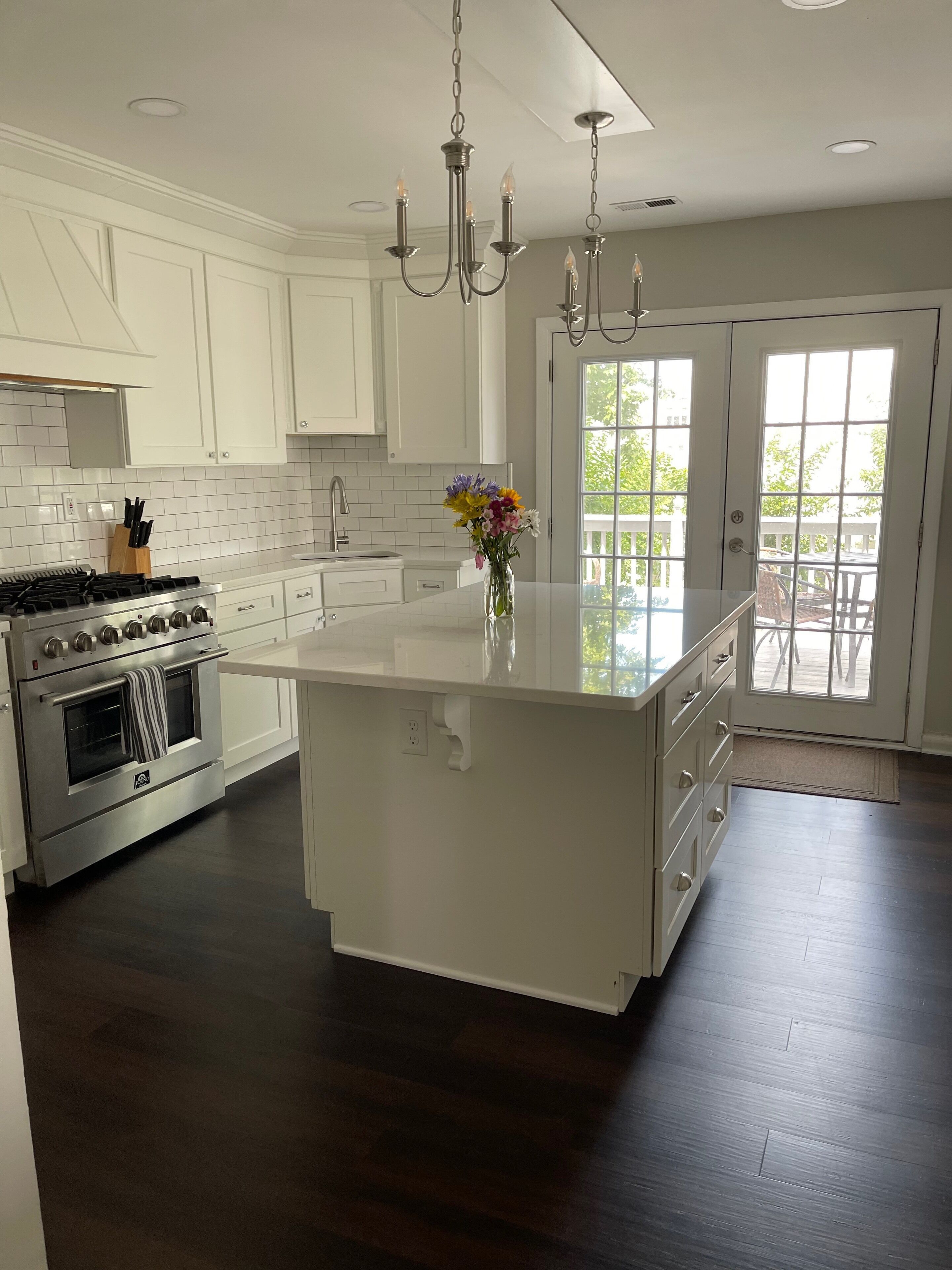 A modern kitchen with white cabinetry, a large island, a gas stove, and a chandelier.