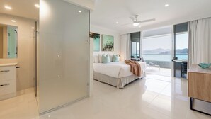 A modern bedroom with a large bed, a balcony with a view of the sea, and a separate bathroom area. - Frangipani Lodge 207, Beachfront Apartment on Hamilton Island (Hamilton Island)