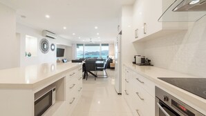 A modern kitchen with a large island, built-in appliances, and a view of the sea. - Frangipani Lodge 207, Beachfront Apartment on Hamilton Island (Hamilton Island)