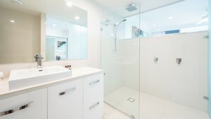 A modern bathroom with a large mirror, a white sink, and a glass-enclosed shower area. - Frangipani Lodge 207, Beachfront Apartment on Hamilton Island (Hamilton Island)