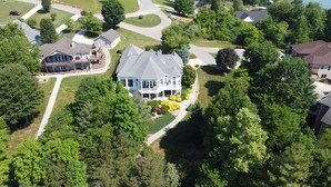 A large, two-story house with a wrap-around porch, surrounded by lush greenery and a well-maintained lawn. - Grand-Escapes on Norris Lake-Available May July3-10, July 17-24, July 31-Aug 14. (La Follette)