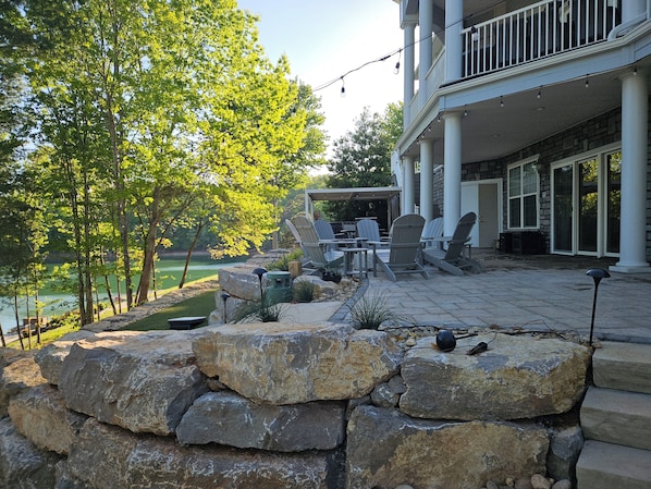 A patio with Adirondack chairs, a stone wall, and a view of a lake.