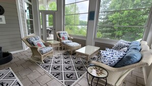 A sunroom with wicker furniture, a patterned rug, and a view of trees and a lake. - Grand-Escapes on Norris Lake-Available May July3-10, July 17-24, July 31-Aug 14. (La Follette)