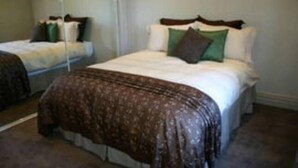 A bedroom with two beds, a large mirror, and a brown patterned bedspread. - Bluebells Cottage Central Albury (Albury)
