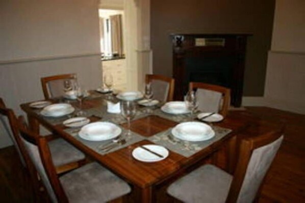 A dining table set with plates, glasses, and cutlery, surrounded by chairs. - Bluebells Cottage Central Albury (Albury)