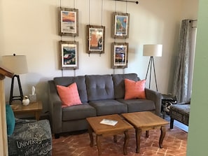A living room with a grey sofa, two wooden coffee tables, a lamp, and framed travel posters on the wall. - Yes it's summer, but Fall is only a few months away!  Book now! (Angel Fire)