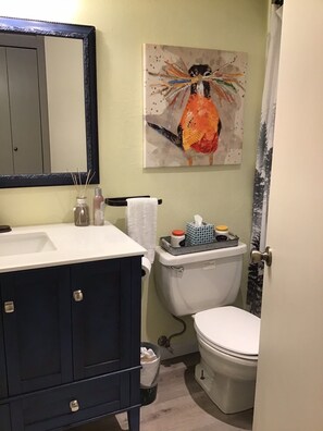Une salle de bain avec un meuble-lavabo bleu foncé, un lavabo blanc, des toilettes et un tableau accroché au mur.