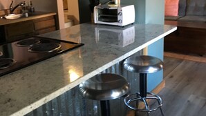 A kitchen with a marble countertop, a toaster, and a sink. There are three stools at the counter.